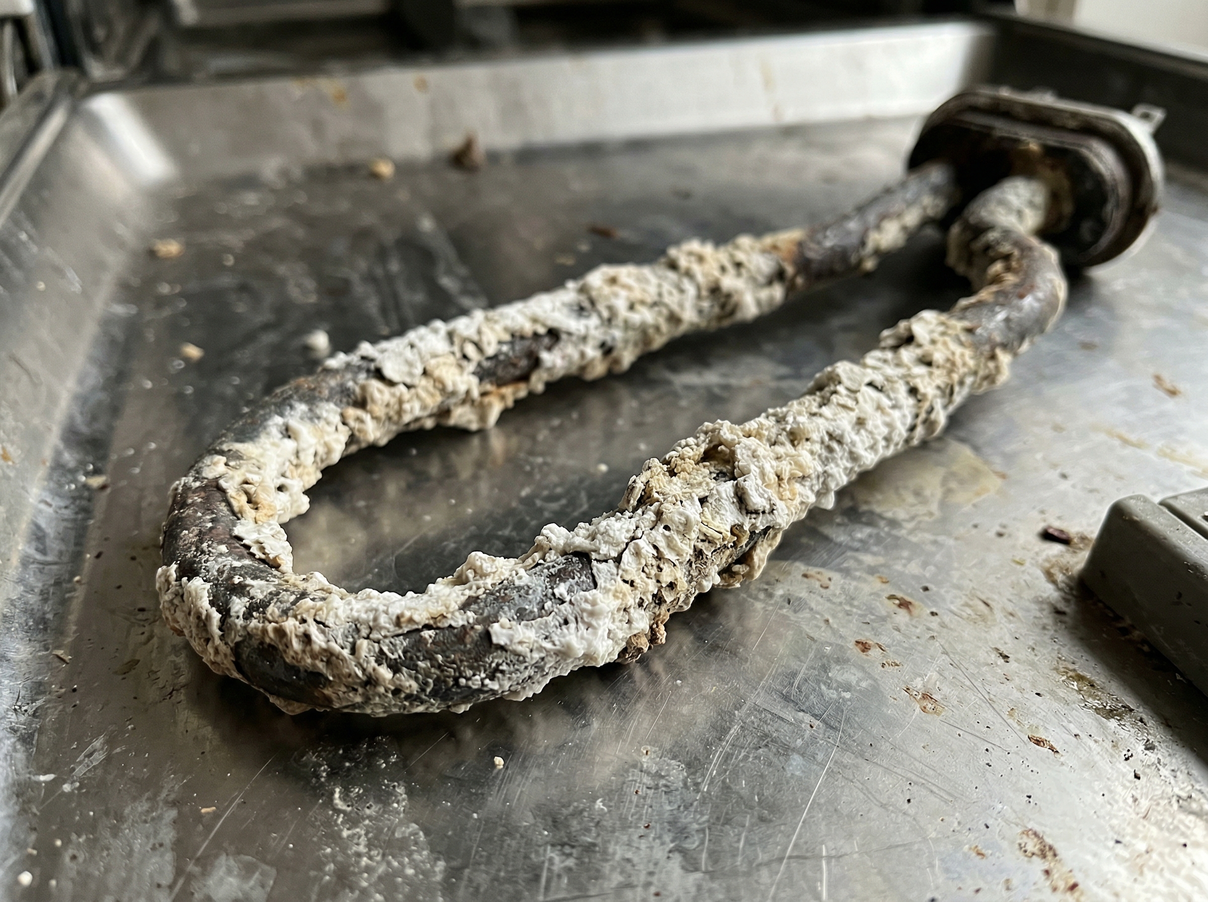 Dishwasher heating element coated in heavy white calcium scale from hard well water